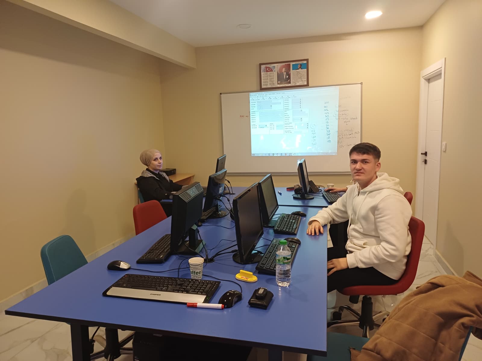 Tahtada tek düzen hesap planı kodları yazılı, kursiyerler bilgisayarlarında kayıt giriyor